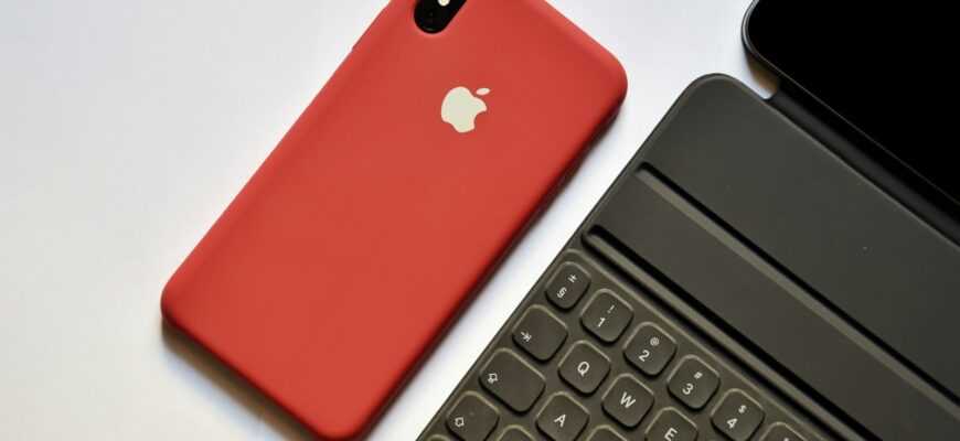 space gray iPhone with red case beside tablet keyboard